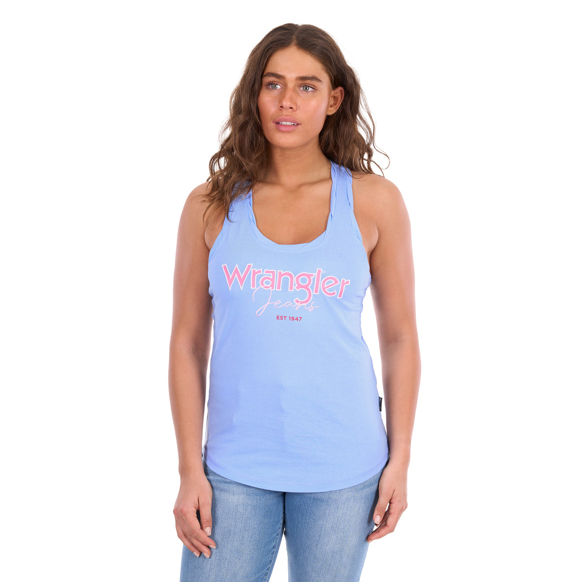 A woman modelling a light blue Wrangler Womens Maya Tank (X6S2508649) with 'Wrangler Jeans' appliqued and embroidered in pink and white across the chest, paired with blue jeans against a plain white background.