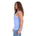A woman in side profile modelling a light blue Wrangler Womens Maya Tank (X6S2508649) with 'Wrangler Jeans' appliqued and embroidered in pink and white across the chest, paired with blue jeans against a plain white background.