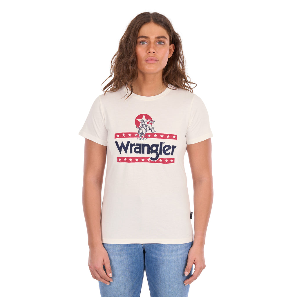 A woman modelling a Wrangler Women's Nora Short Sleeve Tee (XCP2598636) in cream, featuring a red, white, and navy blue graphic logo on the chest, paired with blue jeans against a plain white background.