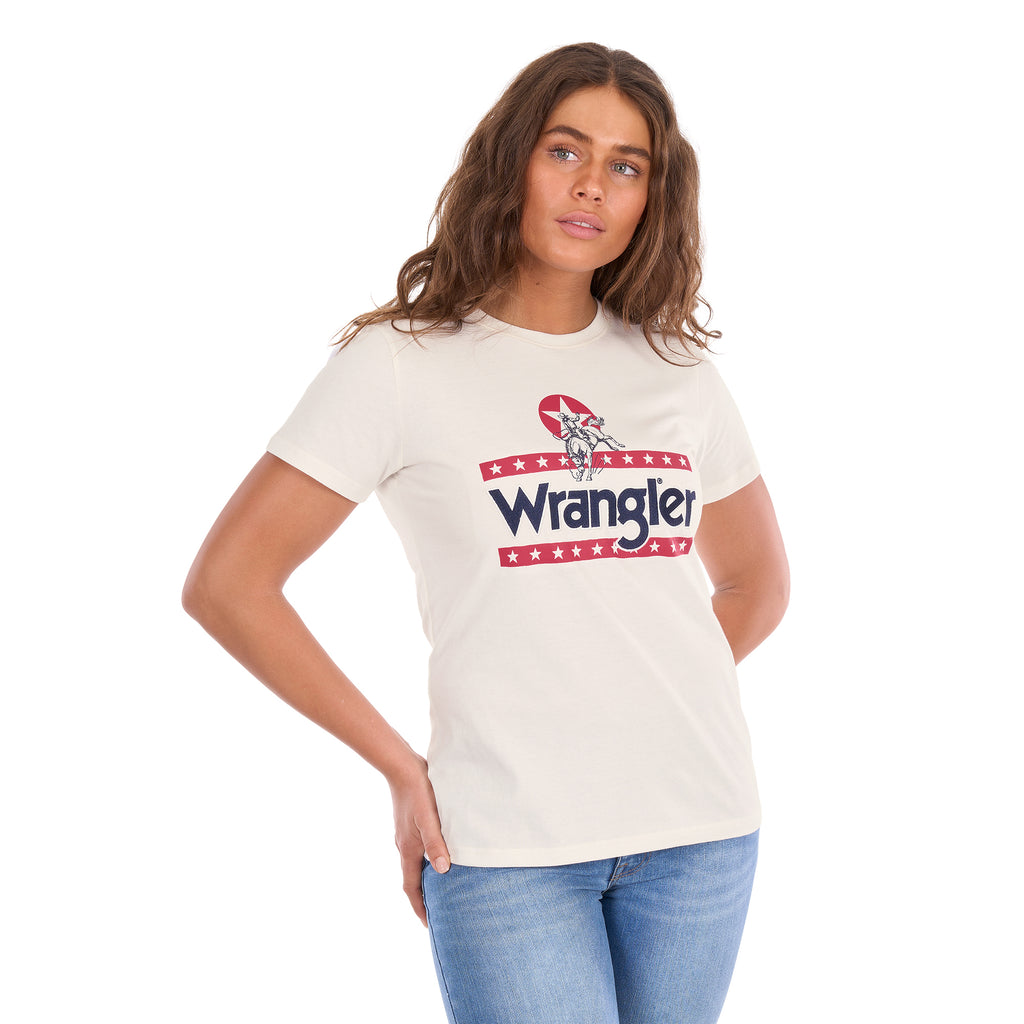 A woman modelling a Wrangler Women's Nora Short Sleeve Tee (XCP2598636) in cream, featuring a red, white, and navy blue graphic logo on the chest, paired with blue jeans against a plain white background.