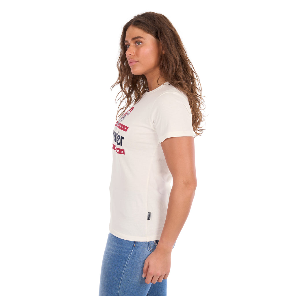A woman in profile modelling a Wrangler Women's Nora Short Sleeve Tee (XCP2598636) in cream, featuring a red, white, and navy blue graphic logo on the chest, paired with blue jeans against a plain white background.