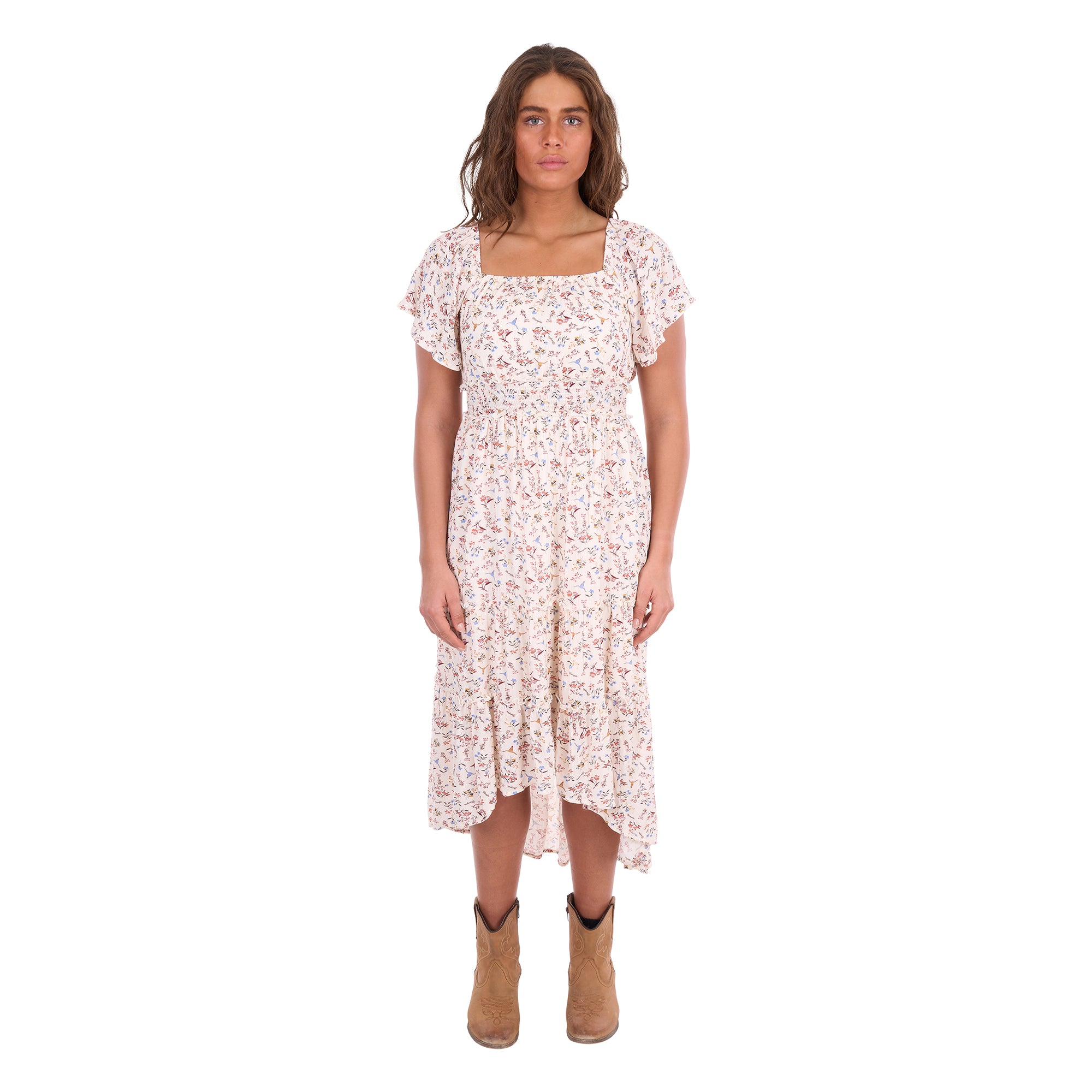 A woman modelling a cream Wrangler Women's Renee Short Sleeved Dress (X6S2407621) with a square neckline and a delicate western floral print on a light cream background, paired with brown ankle boots, set against a plain white background.
