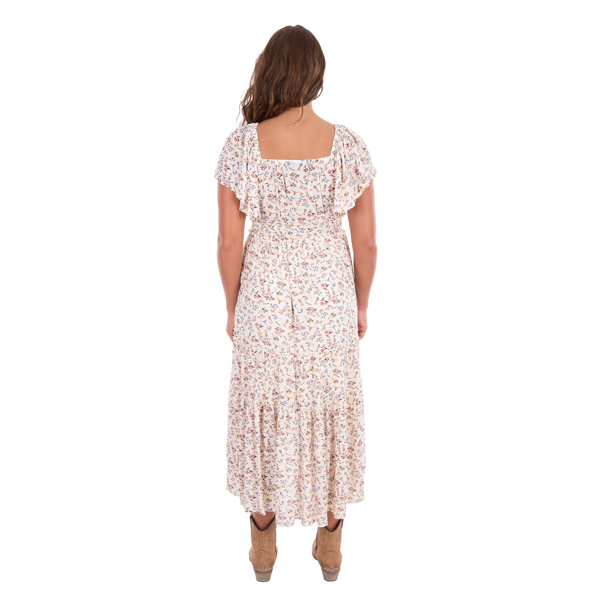 A woman modelling a cream Wrangler Women's Renee Short Sleeved Dress (X6S2407621) with a square neckline and a delicate western floral print on a light cream background, paired with brown ankle boots, set against a plain white background, photographed from behind.