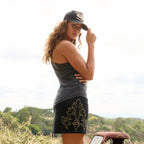 A woman modelling a black Wrangler Women's Rock Denim Mini Skirt (X6S2409725) with silver embroidered floral details on the sides, a Wrangler Jasmine Tank Top, and a Jasmine Trucker Cap, photographed outdoors.