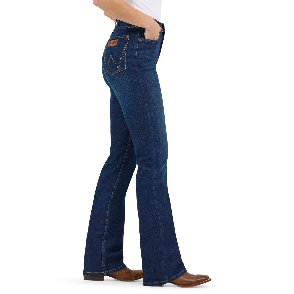 A profile view of a woman shown from the waist down modelling a pair of Kayla blue Wrangler Women's Rodeo Bootcut Jeans (112367606) paired with a white top and brown western boots on a white studio background.