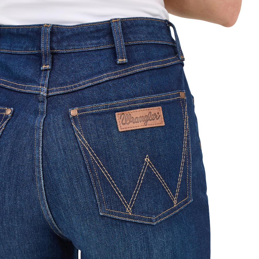 Close up back pocket detail on a pair of Kayla blue Wrangler Women's Rodeo Bootcut Jeans (112367606) paired with a white top on a white studio background.