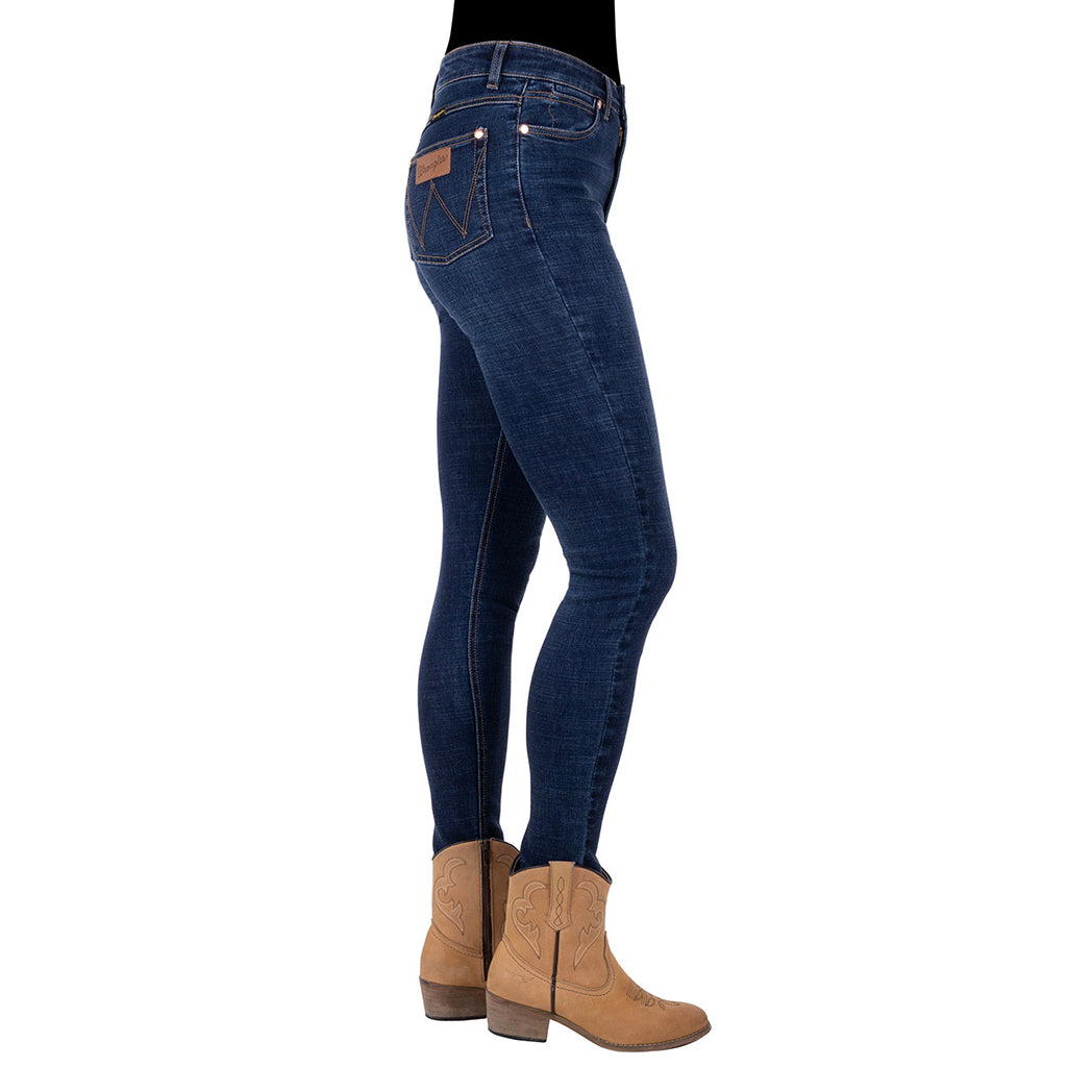 Profile view of a person wearing old indigo blue Wrangler Women's Sierra Skinny Jeans (XCP2238861) with tan cowboy boots against a plain white background.