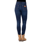 Rear view of a person wearing old indigo blue Wrangler Women's Sierra Skinny Jeans (XCP2238861) with tan cowboy boots against a plain white background.