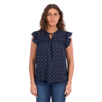 A woman modelling a navy blue Wrangler Women's Sofia Short Sleeve Blouse (X6S2503617) with a small repeating geometric pattern, ruffled cap sleeves, and a keyhole tie neckline, paired with blue jeans against a plain white background.