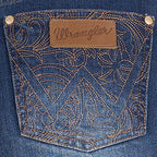 Close-up of an old indigo blue denim Wrangler Women's Summer High Rise Denim Shorts (XCP2412718)  back pocket with intricate gold-toned embroidery, a brown leather patch, and the Wrangler logo.